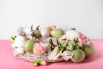 Easter wreath decorated with eggs and flowers on pink table