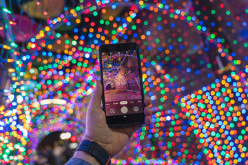Hand holding smartphone and taking a picture of colorful bokeh lights in the background