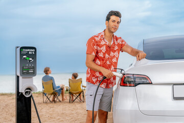 Family vacation trip traveling by the beach with electric car, dad or father recharge EV car while...