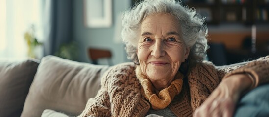 An elderly woman with wrinkles is sitting on a couch, gesture of joy as she smiles happily at the camera, sharing a moment of fun at the event - obrazy, fototapety, plakaty