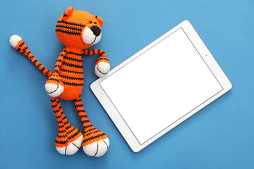 Modern tablet and toy tiger on blue background, flat lay. Space for text