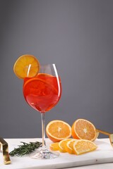 Glass of tasty Aperol spritz cocktail with orange slices and rosemary on white table against gray background, space for text