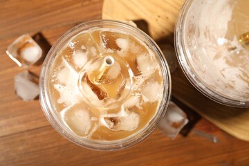 Refreshing iced coffee with milk in takeaway cups on wooden table, flat lay