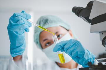 Female researchers are experimenting with pipette dropping a sample into a test tube in an...
