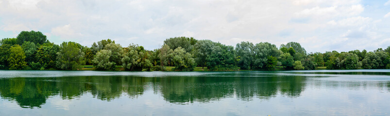 Panoramic view of beautiful lake in park. Landscape with lake, green trees and blue sky.