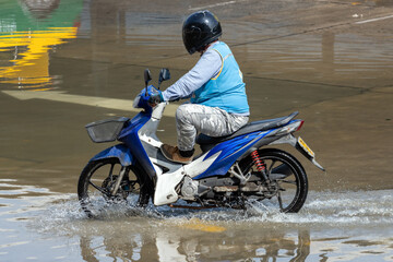 A taxi driver on a motorcycle drives through a flooded street