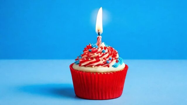 Blue cupcake with red sprinkles and lit candle on a blue background, motion