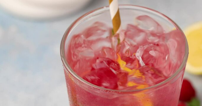 Raspberry lemonade or cocktail with slices of lemon and fresh mint being stirred with a straw