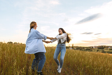 two women friends having fun in a field at sunset