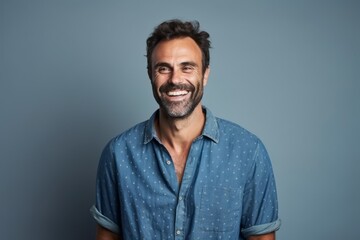 Handsome middle aged man smiling at the camera while standing against a grey background.
