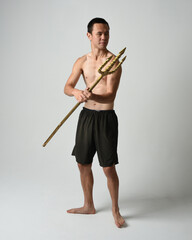 Full length portrait of fit handsome shirtless asian male model,  Holding golden trident weapon,...