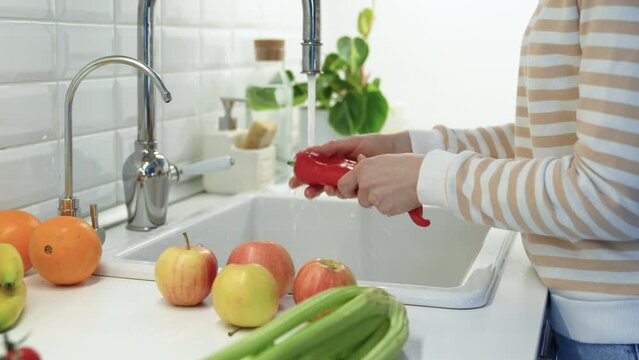 Washing of red ramiro pepper under tap water. Oranges, apples, celery lying on table. Healthy tasty raw sweet fresh fruit and vegetables full of vitamins, used for salad cooking. Natural nutrition