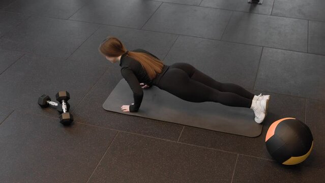 Young caucasian fitness woman doing push ups during training in fitness studio. Top view. Active lifestyle concept.