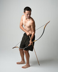 Full length portrait of fit  asian male model,  Holding hunting bow and arrow archery weapon, standing in warrior training action pose, isolated on white studio background.