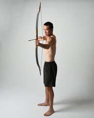 Full length portrait of fit  asian male model,  Holding hunting bow and arrow archery weapon,...