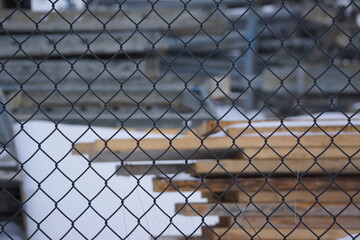 Fastened pile of timber planks on snowy ground, chainlink fence in foreground 