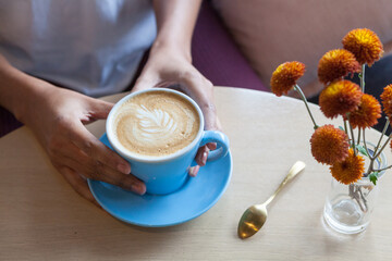 Woman's hands holding a latte in a brightly lit cafe.