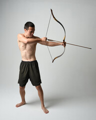 Full length portrait of fit  asian male model,  Holding hunting bow and arrow archery weapon,...