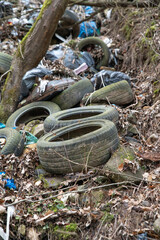 Old used car tires in the forest. Illegal dump of tires in the nature. Environmental pollution.