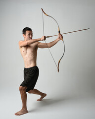Full length portrait of fit  asian male model,  Holding hunting bow and arrow archery weapon,...