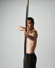 Full length portrait of fit  asian male model,  Holding hunting bow and arrow archery weapon,...