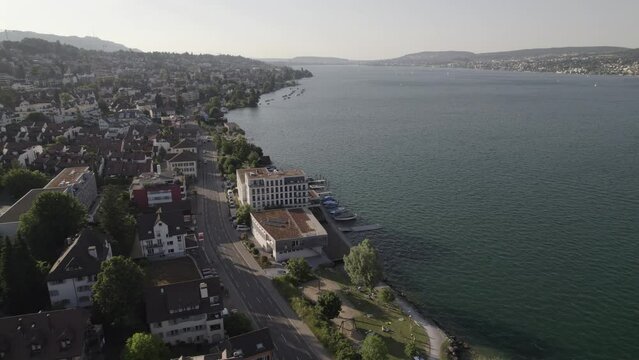 Drone shot flying near the city of Thalwil at the Zurich Lake in Switzerland  on a sunny day with water and boats around the shore and white houses in the city LOG