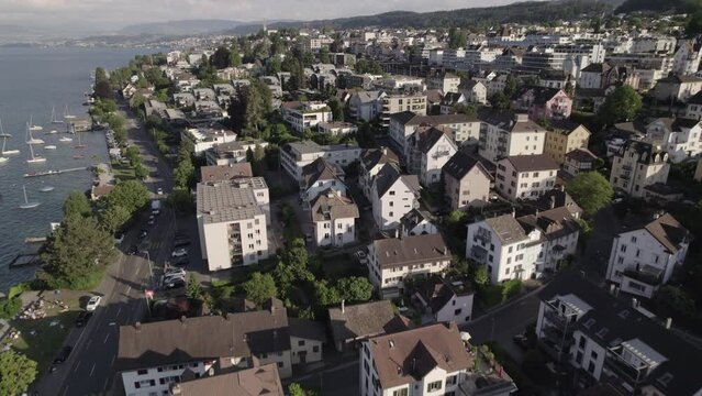 Drone shot flying near the city of Thalwil at the Zurich Lake in Switzerland  on a sunny day with water and boats around the shore and white houses in the city LOG