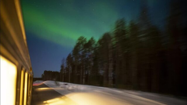Outside view of train traveling through a snowy forest with green northern lights lighting up the sky