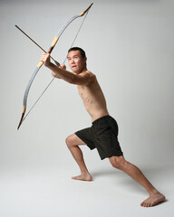 Full length portrait of fit  asian male model,  Holding hunting bow and arrow archery weapon,...