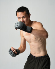 Close up portrait of fit  asian male model, shirtless with muscles. Wearing gym shorthand boxing gloves, gestural punching pose. Isolated on a white studio background.