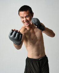 Close up portrait of fit  asian male model, shirtless with muscles. Wearing gym shorthand boxing gloves, gestural punching pose. Isolated on a white studio background.