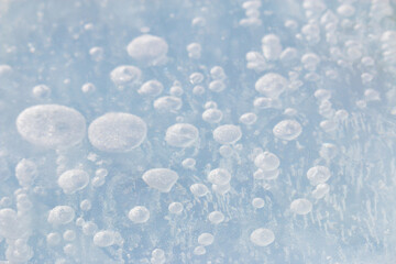 Natural methane gas bubbles frozen in pale blue ice background