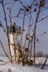 Old lighthouse in winter on a background of blue sky and bushes