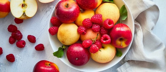 A dish with red and yellow apples and raspberry seen from above in bright lighting.