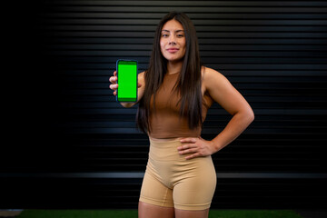 Athlete woman smiling shows the green screen of her cell phone, to create an application