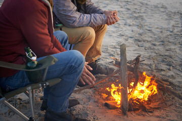 Campfire, friends and hands of men by the beach at sunset with vacation and camping. Ocean, outdoor...