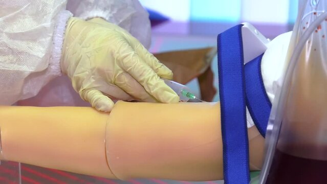 Woman makes an injection in the arm of a mannequin. Hand of a medical plastic mannequin for the practice and training of young doctors on a simulator.