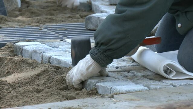 Laying paving slabs close-up. Worker laying stone paving slab. Laying tiles in the city park garden . Tiler worker laying tiles on foundation of building outside. Hands of worker with hammer close-up
