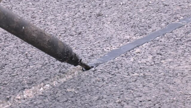 Road surface restoration work in the worker performs on road patches work the repair of cracks by filling sealing with coated by bitumen emulsion. Asphalt with filled cracks. Asphalt repairing.
