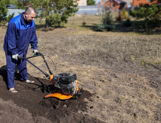 A man works in a vegetable garden in early spring. Digs the ground.  Works as a cultivator, walk-behind tractor.