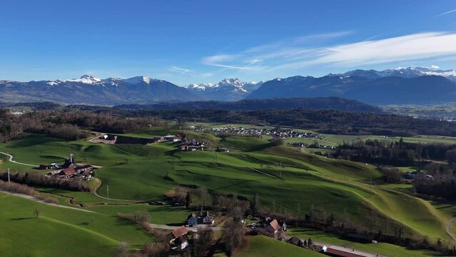The glarner alps shadowing jona village in switzerland, lush green fields under clear blue sky, aerial view