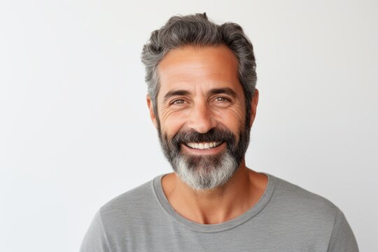 Portrait of handsome middle-aged man with gray hair and beard looking at camera and smiling while standing against grey background