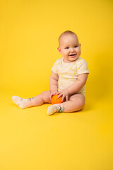 Beautiful baby girl holds orange sitting in studio on yellow background.