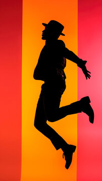 Energetic dancer wearing hat dancing silhouetted against orange and yellow background, modern lifestyle