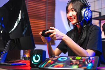 Happy asia girl gamer wear headphone competition play video game online with computer colorful neon light in living room at night © joyfotoliakid