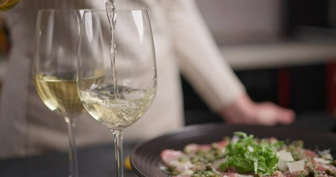 Woman pours white win onto glass to complement dinner with tuna carpaccio