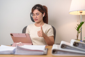 young smart woman having Video conference call via Tablet pad. businesswoman showing Thumb Up sign while Online Meeting with documents at home or office night. Teleconference and Technology concept