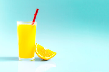 A bright photo of natural orange juice in a transparent glass with a slice of orange and a bright red tube on a light background