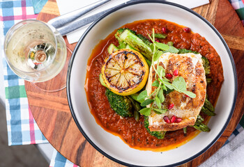 Grilled Barramundi with a side of broccoli and asparagus, served in a white round bowl with grilled lemon and a white wine.