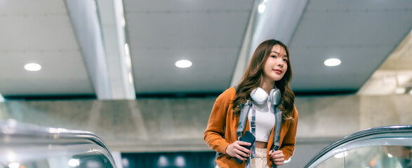 Young asian woman in international airport terminal or modern train station. Backpacker passenger female commuter walking on escalator - Powered by Adobe
